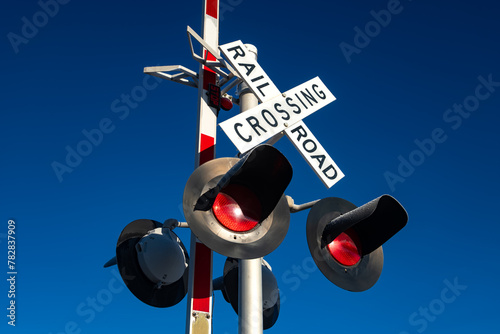 Signs and red warning lights at an American railroad crossing in Arizona. White cross with the inscription "Railway crossing" and flashing lights from a worm's eye view with a deep blue morning sky.