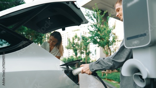 Young couple travel with EV electric car charging at green sustainable home in summer shows urban sustainability lifestyle by green clean rechargeable energy of electric vehicle innards