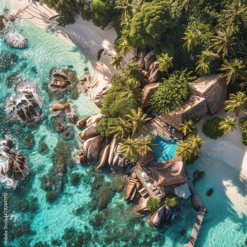 A white sandy beach  palm trees and a blue ocean with large rocks with a house and pool.
