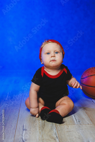 Portrait of a 7-month-old baby in a black bodysuit with a basketball. Sports for kids. Cotton clothes for babies