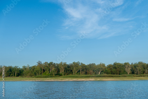 Horizontal and landscape view of river. With background of coast is covered with grass and forests. Under blue sky and  soft white clouds.