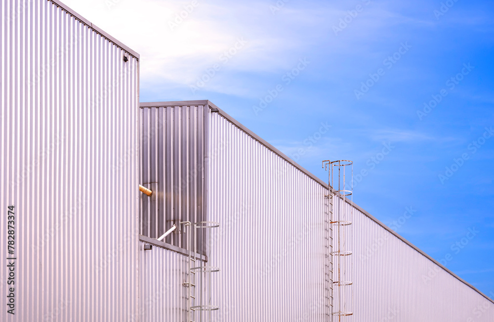 Two metal industrial warehouse buildings with cylinder ladders on aluminum corrugated wall against blue sky background, low angle and perspective side view 