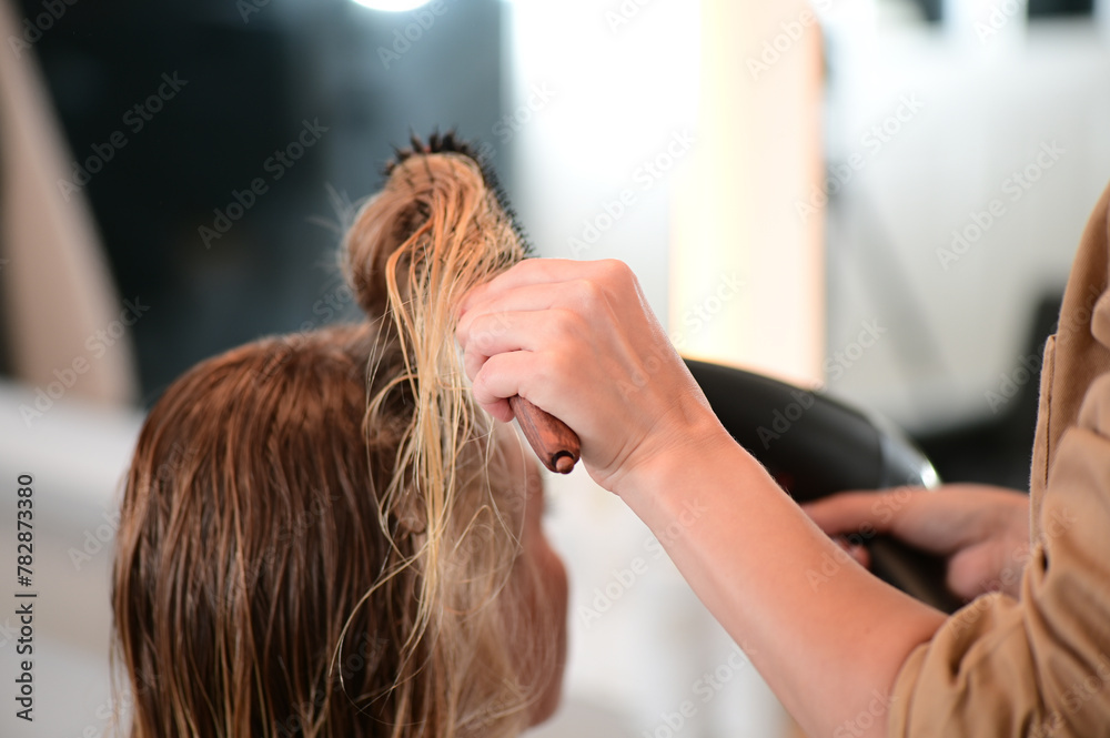 Naklejka premium Hairdresser drying and brushing wet hair of a blonde client in a hair salon