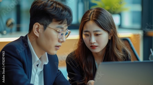 An Asian man and a woman sitting at a desk, collaborating on a project or task using a notebook computer Fictional Character Created by Generative AI.