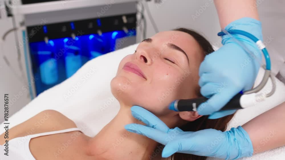 Close-up of a cosmetologist's hands polishing and cleansing the skin of a middle-aged woman's face using a vacuum machine. Concept of skin care, rejuvenation and cosmetology.