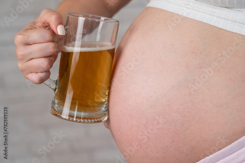 Faceless pregnant woman holding a glass of beer.