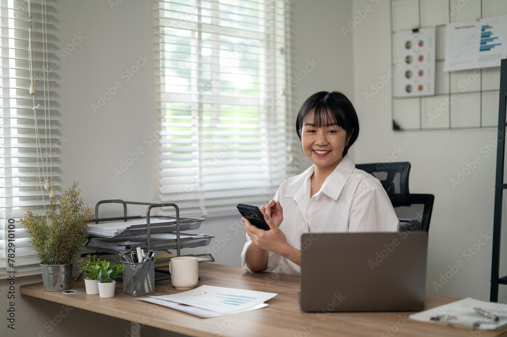 Cheerful businesswoman in white shirt using smartphone with laptop and documents on her office desk. Cheerful businesswoman in white shirt using smartphone with laptop and documents on her office desk.