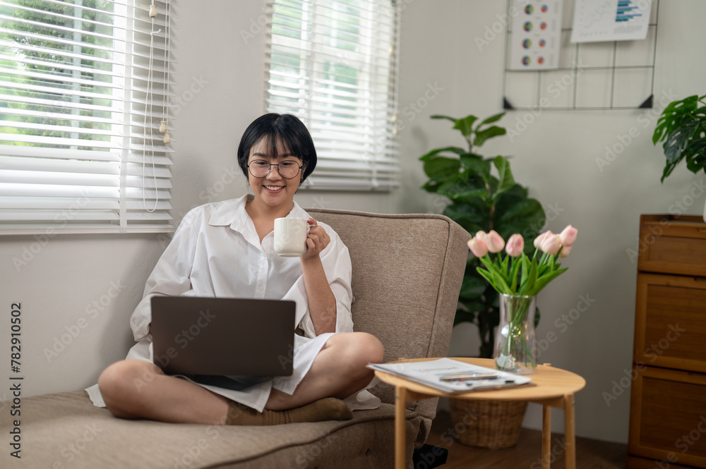 An adult woman sips her coffee while engaging with a laptop in a bright home office, reflecting a moment of tranquility amidst a busy workday.