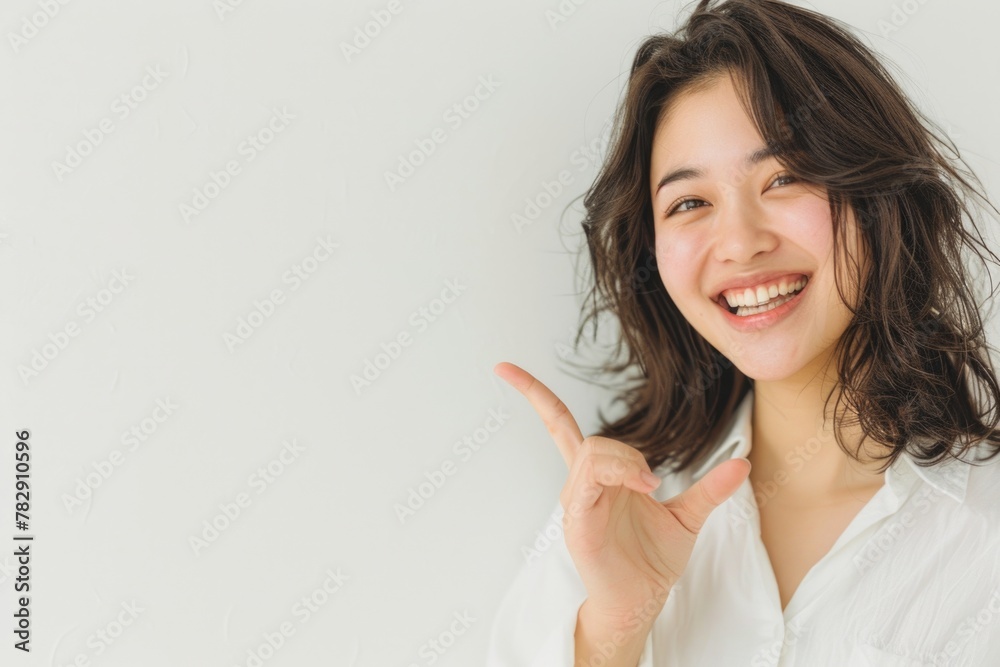 A beautiful Asian woman is smiling, showing with finger, wearing white against a white background in the style of professional photography with sharp focus. A beautiful Asian woman is smiling, showing with finger, wearing white against a white background in the style of professional photography with sharp focus.