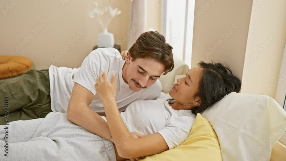 Interracial couple, a man and a woman, share intimate moments laughing and cuddling in a cozy bedroom. Interracial couple, a man and a woman, share intimate moments laughing and cuddling in a cozy bedroom.