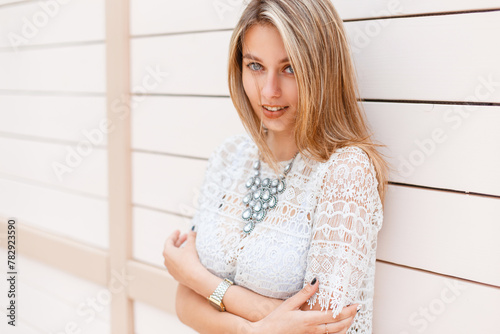 Fashion beautiful hipster woman in a stylish white lace top stands near a wooden wall