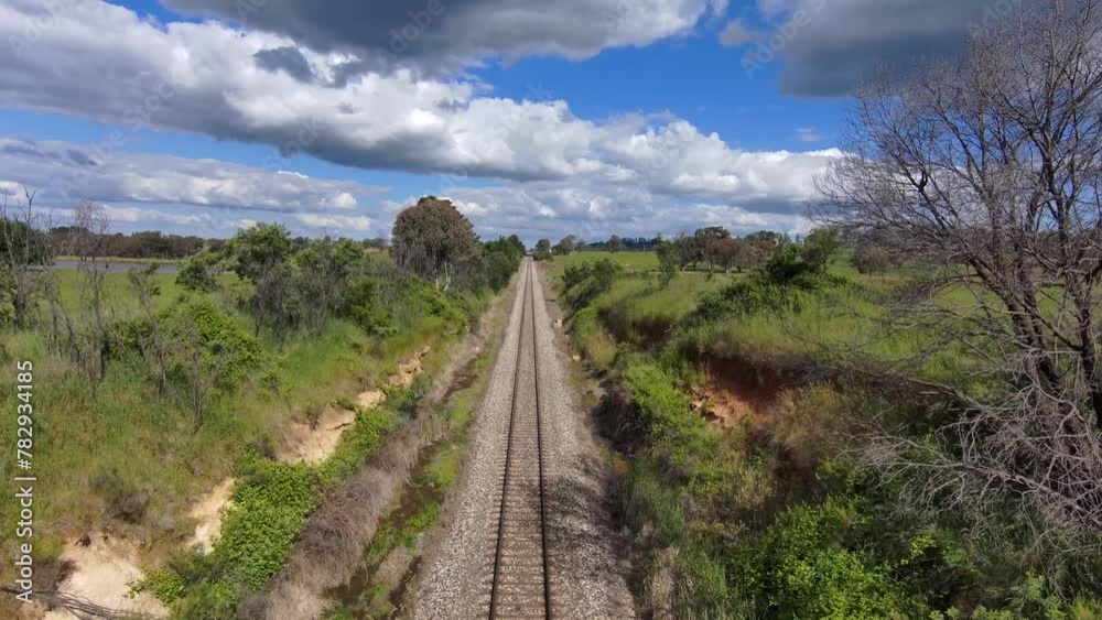 Drone view over a railroad between green fields under a cloudy sky Drone view over a railroad between green fields under a cloudy sky
