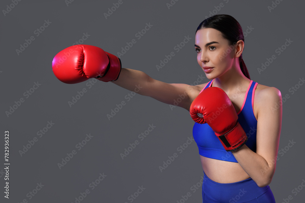 Beautiful woman wearing boxing gloves training in color lights on grey background Beautiful woman wearing boxing gloves training in color lights on grey background