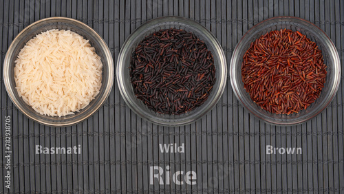 Three transparent bowls display different rice varieties - Basmati, Wild, and Brown. The assortment represents diverse grains used in international cuisine.