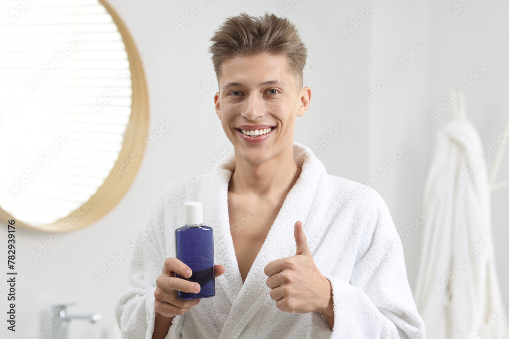 Young man with mouthwash showing thumbs up in bathroom Young man with mouthwash showing thumbs up in bathroom