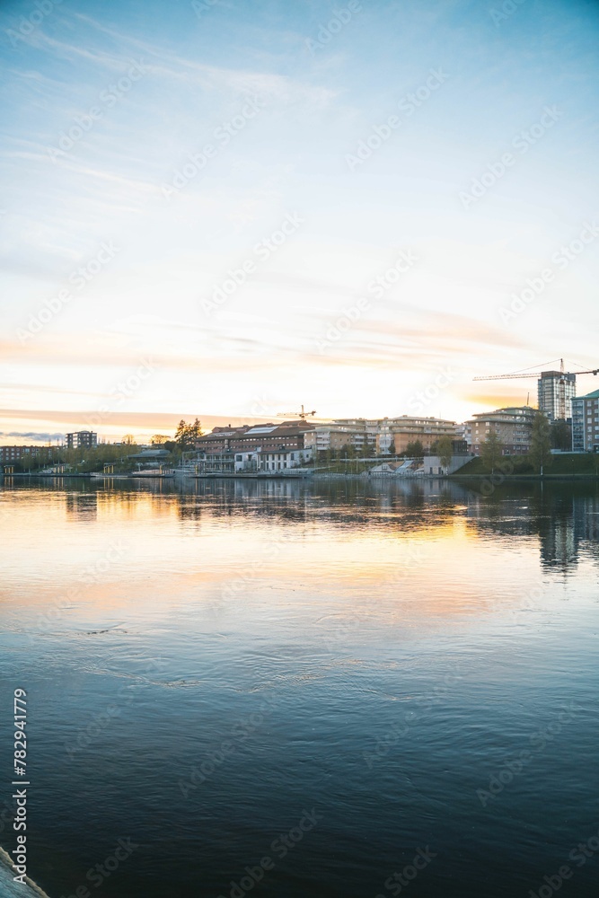 Vertical shot of a peaceful river at sunset with town architecture, Skelleftea, Sweden