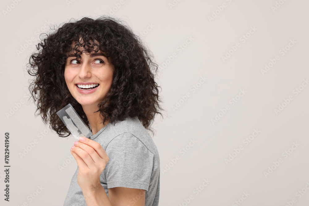 Young woman holding teeth whitening strips on light grey background, space for text Young woman holding teeth whitening strips on light grey background, space for text