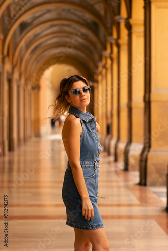 Immersed in the enchanting ambiance of Bologna's renowned porticoes, a young woman elegantly poses for a captivating photo. 