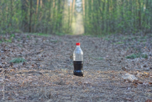 one plastic bottle with a black drink lemonade stands on gray ground on a road in the spring forest
