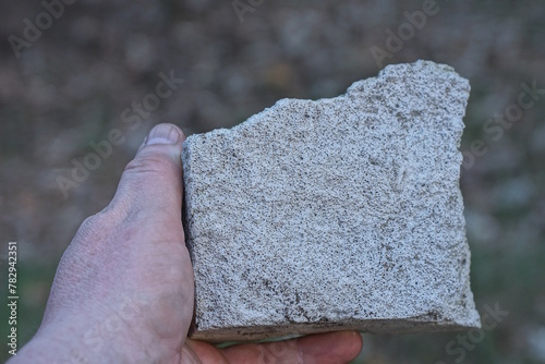 a man hand holds a large gray white piece of stone on a summer street