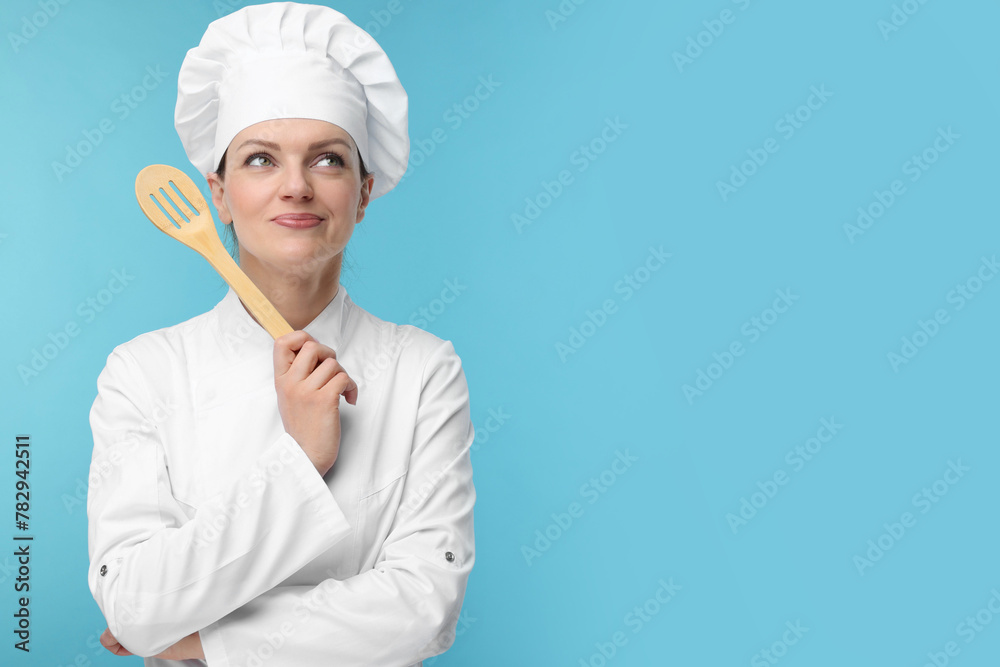 Happy chef in uniform holding wooden spatula on light blue background, space for text Happy chef in uniform holding wooden spatula on light blue background, space for text