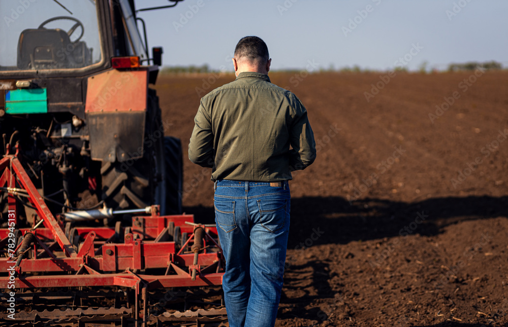 Rear view of mature farmer standing in field preparing to cultivate the land with a tractor. Rear view of mature farmer standing in field preparing to cultivate the land with a tractor.