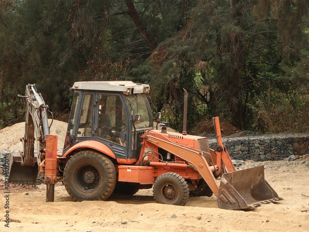 Big truck working on the sandy ground in a construction site against green trees Big truck working on the sandy ground in a construction site against green trees