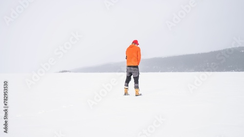 Man with an orange winter Jacket standing on a snow-covered hill