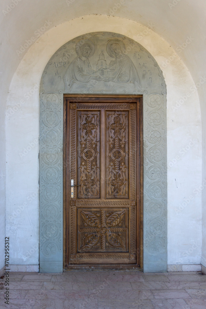 Carved wooden door of the Saint Peter and Paul monastery. Carved stone arch with patterns and bas-relief of saints. View from inside of the church. Georgia