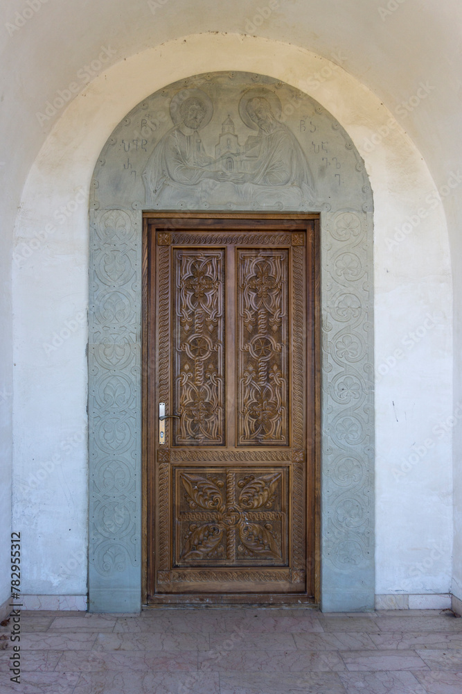 Carved wooden door of the Saint Peter and Paul monastery. Carved stone arch with patterns and bas-relief of saints. View from inside of the church. Georgia Carved wooden door of the Saint Peter and Paul monastery. Carved stone arch with patterns and bas-relief of saints. View from inside of the church. Georgia