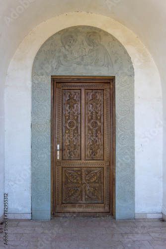 Carved wooden door of the Saint Peter and Paul monastery. Carved stone arch with patterns and bas-relief of saints. View from inside of the church. Georgia