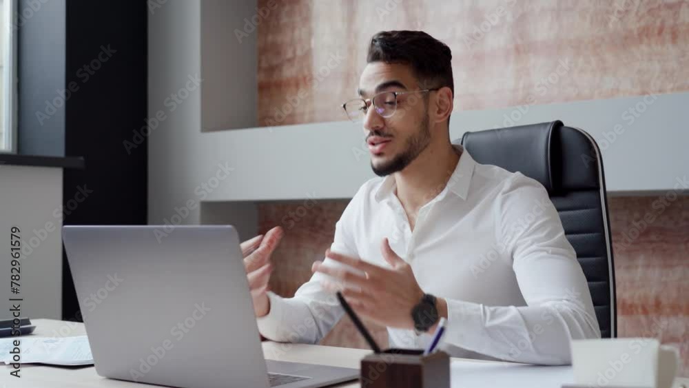 Busy young Arabic business man hr manager team leader professional executive working in office looking at laptop computer talking having video conference call virtual online hybrid work meeting.