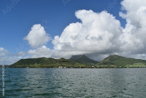The rocky sea coast with a mountain peak in clouds, a reflection of sunlight on the water's surface