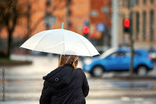 Young woman with white umbrella waiting signal for cross walk during rain. Alone woman stands with white umbrella, rear view. Urban rainwalk.
