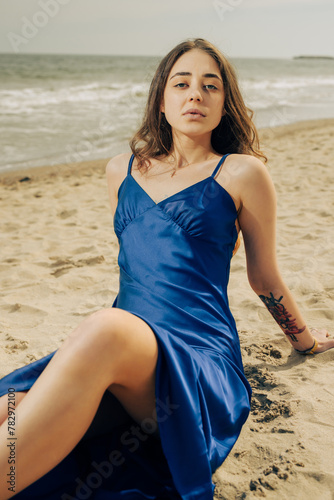 Pretty woman in blue dress sitting on the beach