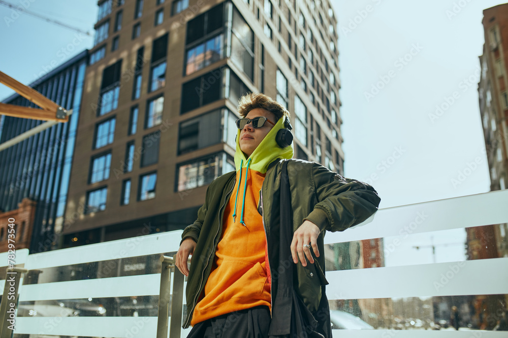 Young cool attitude man, student posing against urban, city views. model dressed trendy, neon oversized clothes. Concept of street fashion and urban style, modern lifestyle, gen Z, self-expression. Young cool attitude man, student posing against urban, city views. model dressed trendy, neon oversized clothes. Concept of street fashion and urban style, modern lifestyle, gen Z, self-expression.