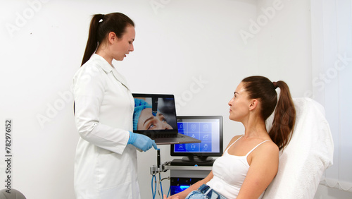 The cosmetologist shows the client a video of the hydrolifting procedure and conducts a consultation. A beautiful woman consults with a cosmetologist. Concept of anti-aging, cosmetology, beauty, facia