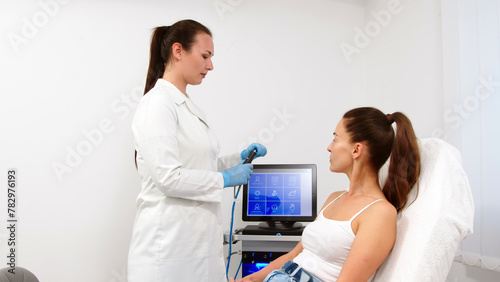 A female cosmetologist-dermatologist talks to a client sitting in a comfortable salon chair. Consultant cosmetologist advises on the facial hydrolifting procedure. Professional inspection.