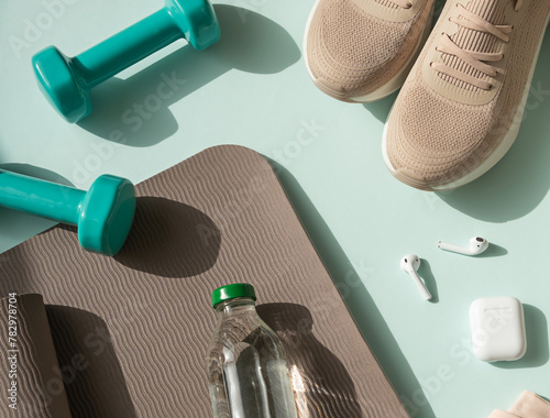 Sport or workout concept flat lay with blue dumbbells, yoga mat and white wireless headphones on the blue background.