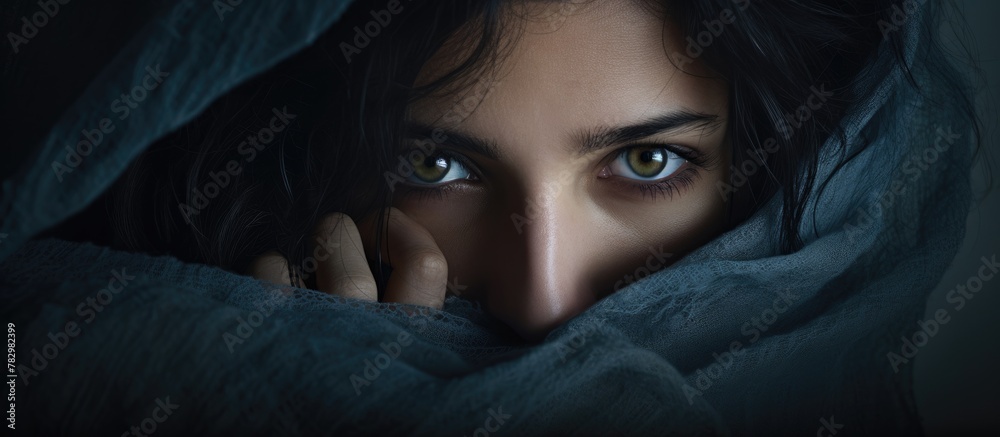 Woman with dark hair and blue eyes concealing beneath blanket - obrazy, fototapety, plakaty 