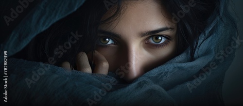 Woman with dark hair and blue eyes concealing beneath blanket