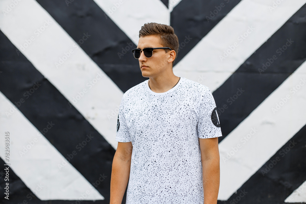 Stylish handsome man with a hairstyle with classic sunglasses in a white T-shirt against a black white wall Stylish handsome man with a hairstyle with classic sunglasses in a white T-shirt against a black white wall