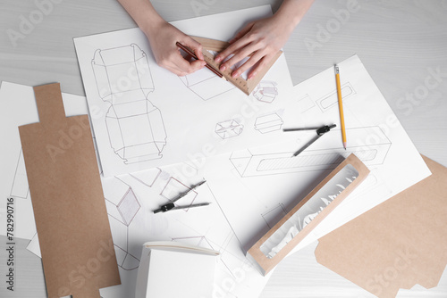 Woman creating packaging design at light wooden table, top view