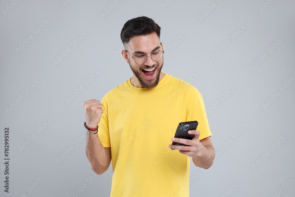 Happy young man using smartphone on grey background Happy young man using smartphone on grey background