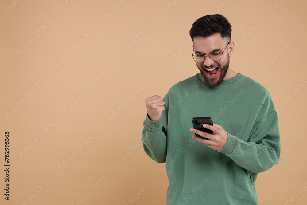 Happy young man using smartphone on beige background, space for text Happy young man using smartphone on beige background, space for text