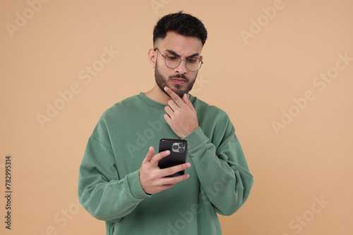 Handsome young man using smartphone on beige background © New Africa
