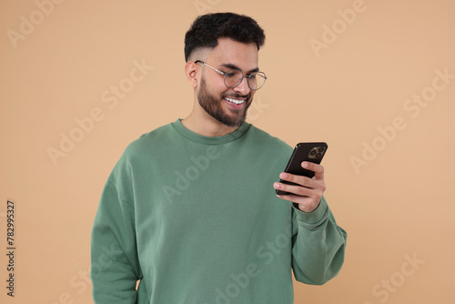 Happy young man using smartphone on beige background © New Africa