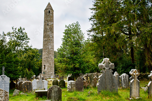 Stone round tower and some ruins of a monastic settlement originally built in the 6th century in Glendalough valley, County Wicklow, Ireland on sunny day