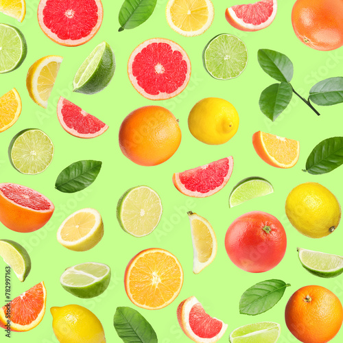 Many different fresh citrus fruits falling on light green background