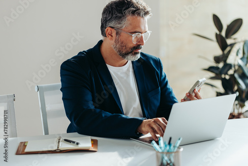 Focused businessman using laptop and smartphone in office